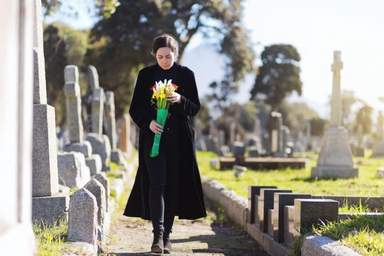 lady holding flowers mourning at a cemetery 