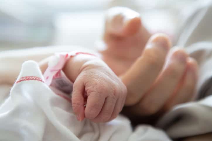 A newborn baby with vacuum extraction complications clutching their parent's finger with their hand