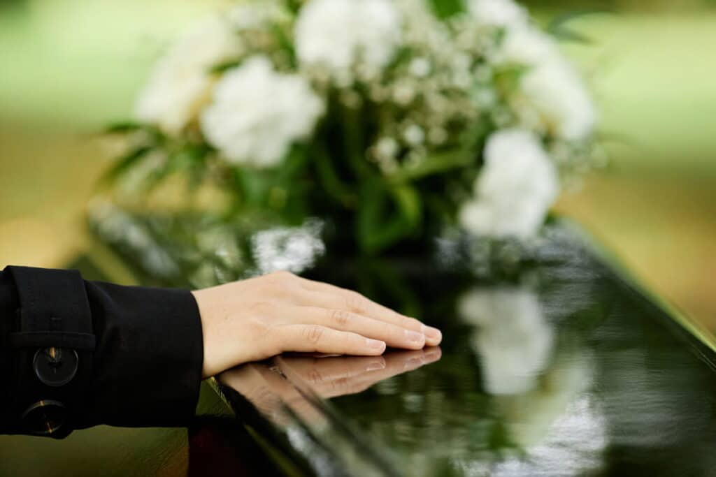 A hand resting on a casket with white flowers after a wrongful death.