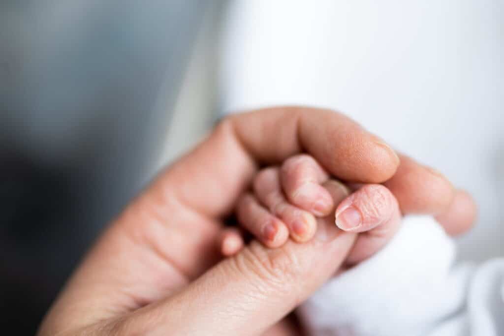 A newborn's hand wrapped around their parent's thumb.