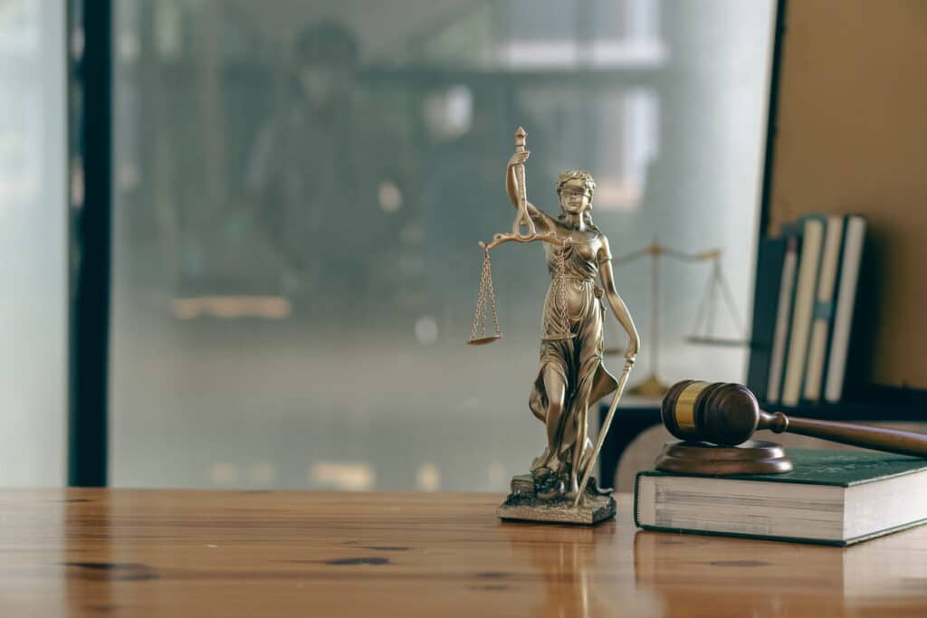 Lady Justice statue next to a book and a gavel on a burn injury attorney's desk.