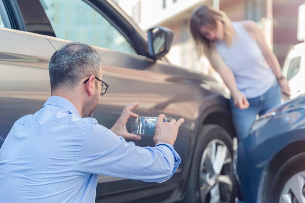 Two people inspecting the damage on their vehicles after a car accident. The one is taking photos.