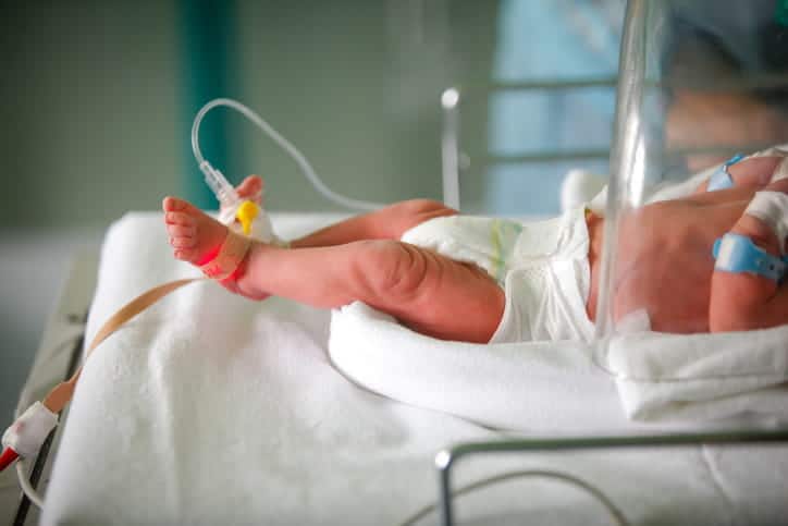 A newborn in a hospital bed shown from the chest down. 