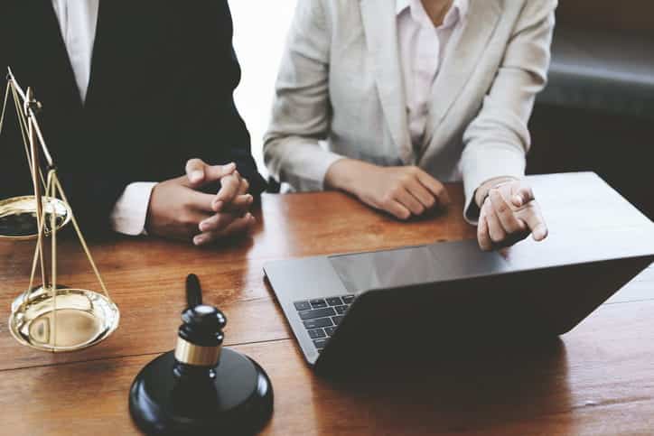 Two personal injury lawyers reviewing a case on a laptop. On the desk in front of them is the scales of justice and a gavel. 