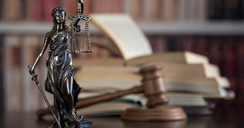 A Lady Justice statue in front of a gavel and a stack of books. 