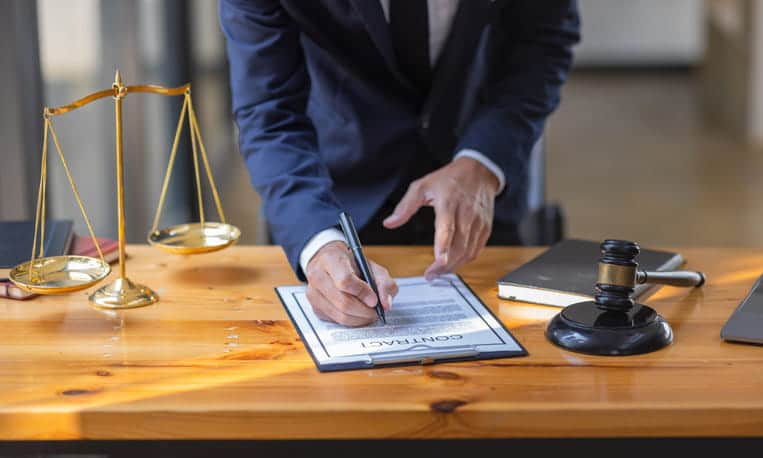 A birth injury lawyer working on a contract at his desk. Next to him is the scales of justice, a gavel, and a book.