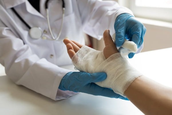 A doctor wraps guaze around a burn injury on a patient's hand. 